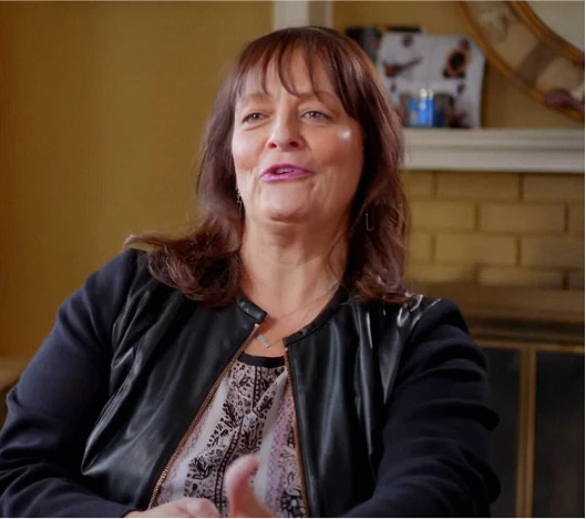 A woman in a black leather jacket sitting in a chair.